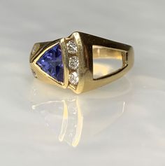 Tanzanite Ring, Trillion Cut Ring, Tanzanite Engagement Ring, Trillion Tanzanite Ring, Geometric Gemstone Ring, Gemstone Engagement Ring A fascinating and shapely vintage tanzanite ring boasting a 1.53 carat trillion cut tanzanite uniquely set on an angle surrounded by sparkling white diamonds weighing 0.48 carats set in solid 14k yellow gold with a modern asymmetric design. *Ring size: US 6 3/4 *Ring weight: 6.54 grams *Complimentary resizing is available up to 3 sizes larger or smaller than st Formal Tanzanite Trillion Cut Ring, Fine Jewelry Yellow Gold Trillion Cut Sapphire Ring, Trillion Cut Diamond Ring With Gemstone For Formal Occasions, Formal Trillion Cut Diamond Ring With Gemstone, Fine Jewelry Trillion Cut Sapphire Ring With Accent Stones, Fine Jewelry Multi-stone Trillion Cut Ring, Sapphire Gemstone Ring, Trillion Cut, Trillion Cut Sapphire Gemstone Ring, Formal Rings With Accent Stones In Trillion Cut