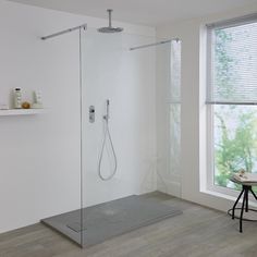 a bathroom with white walls and wooden flooring has a walk in shower that is next to a window