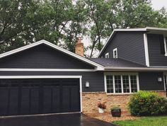 a black house with two garages and trees in the background