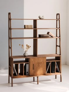 a wooden shelf with books and vases on it in front of a white wall