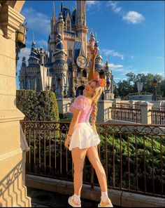 a woman in a pink shirt and white skirt standing next to a castle