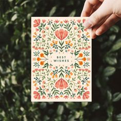 a person holding up a card with the words best wishes in front of some plants