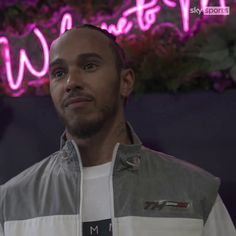 a man standing in front of a neon sign with his hand on his hip and looking off to the side