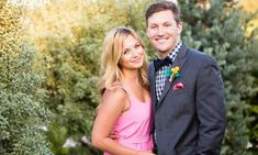 a man and woman standing next to each other in front of some bushes, smiling at the camera