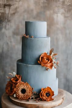 a three tiered blue cake with orange flowers on the top and bottom, sitting on a wooden stand