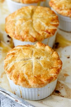 four pies sitting on top of a cutting board next to a knife and fork