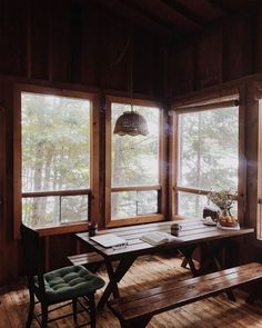 a table with two benches in front of three windows and a lamp hanging from the ceiling