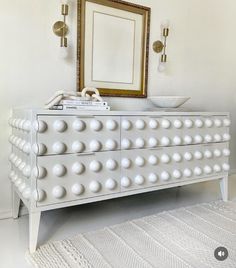 a white dresser sitting in front of a mirror on top of a floor next to a rug