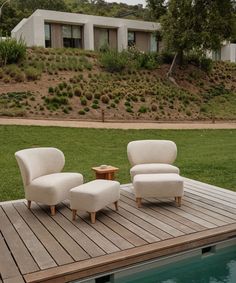 two white chairs sitting on top of a wooden deck next to a swimming pool in front of a house