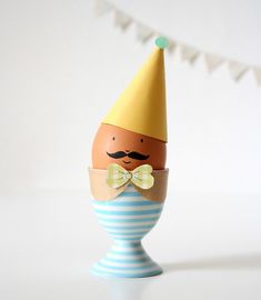 an egg wearing a party hat and bow tie is in a blue striped egg cup