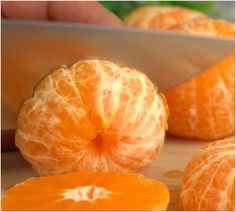 someone slicing an orange with a knife on a cutting board next to other sliced oranges