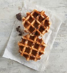 two waffles sitting on top of a piece of parchment paper next to chocolate chips