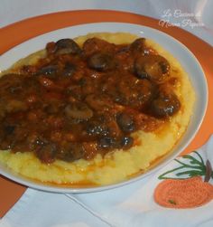 a white plate topped with mashed potatoes covered in mushroom gravy on top of an orange and white table cloth