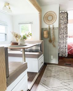 a living area with a couch, table and window in the back ground next to a bed