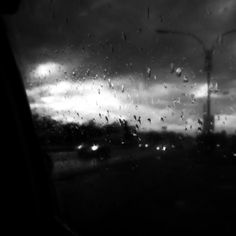 black and white photo of rain on windshield with street light in distance from car window