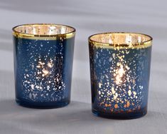 two blue candles with gold speckles are sitting on a gray tablecloth covered surface