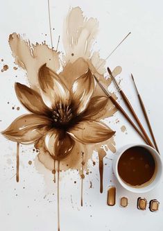 a coffee cup next to some paint brushes and a flower on a white table top