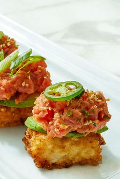 two pieces of food on a white plate with green garnish and tomato slices