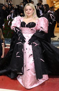 lady in black and pink gown with feathers on the floor at red carpet, posing for camera