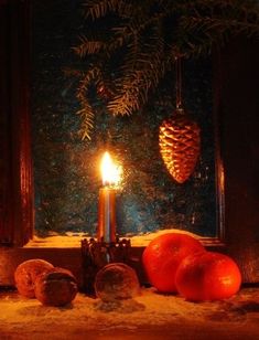 a lit candle sitting on top of a window sill next to oranges and pine cones