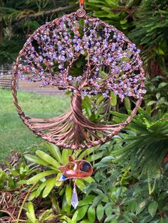 a metal tree with purple flowers hanging from it's sides in a garden filled with green plants