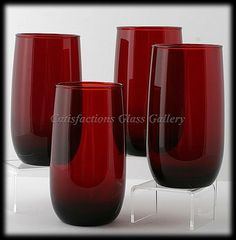 three red glass vases sitting on top of a clear shelf