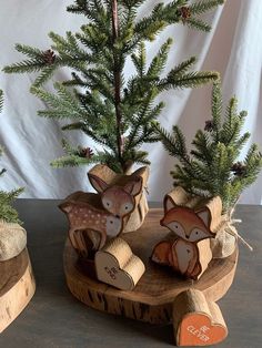 two small wooden deer ornaments sitting on top of a piece of wood next to a pine tree