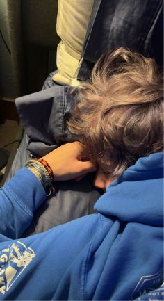 a person laying on top of a bed with their head in his hands and wearing a blue jacket