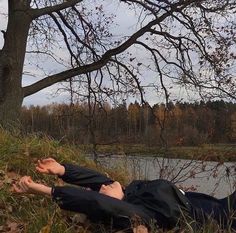 a man laying on the ground in front of a tree next to a body of water