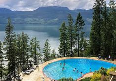 an outdoor swimming pool surrounded by pine trees and overlooking a lake with mountains in the background