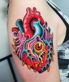 a colorful heart tattoo on the left arm and shoulder, with an eye in the center