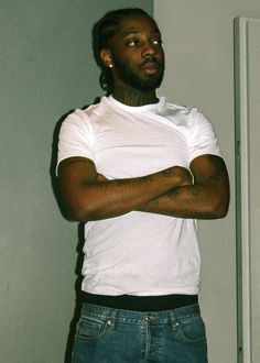 a man with his arms crossed standing in front of a white wall and refrigerator freezer