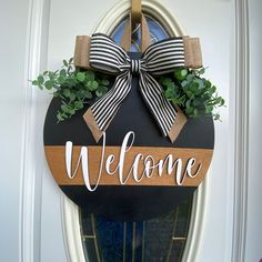 a welcome sign hanging on the front door with greenery and ribbon tied around it