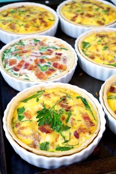 several different types of food in pie pans on a baking sheet with green garnishes