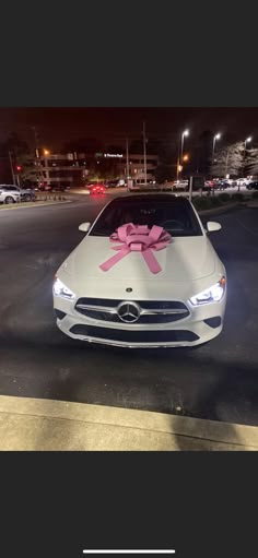 a white car with a pink bow on it's hood parked in a parking lot