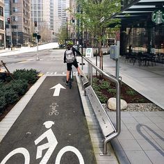 a person riding a bike down a street next to a sidewalk with an arrow painted on it