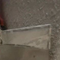 a red object sitting on the ground next to a metal pole and some water droplets