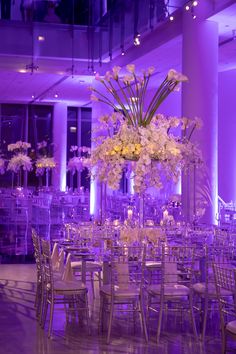 the tables are set with white flowers and silver chairs for an elegant wedding reception in purple lighting