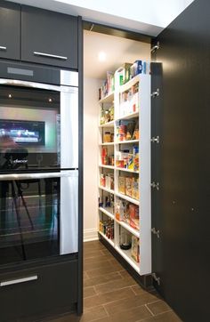 an oven and pantry in a kitchen with tile flooring, black cabinets and white walls