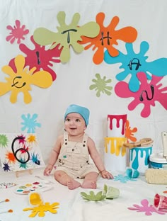 a baby sitting on the floor in front of paper flowers