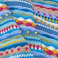 a crocheted blanket is laying on top of a bed with multicolored stripes