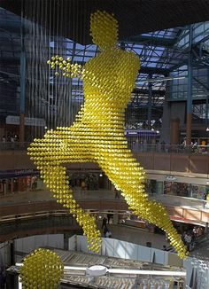 a large yellow sculpture is in the middle of a mall