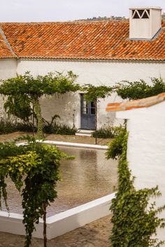 an old white building with red tiled roof and trees in the foreground, on a rainy day