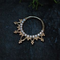 a close up of a gold ring on a black surface with flowers in the background