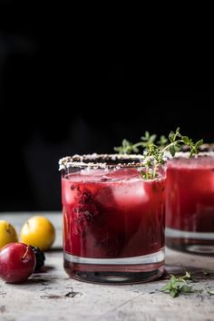 two glasses filled with red liquid and garnish next to lemons on a table