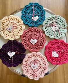 six crocheted doily with hearts tied to them on a plate, all in different colors