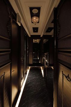 an empty hallway leading to another room with lights on the ceiling and dark wood paneling