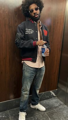 a man with an afro standing in front of a wall holding a bottle of water