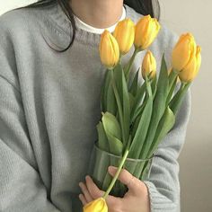 a woman holding a vase filled with yellow tulips in front of her face