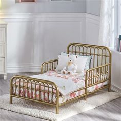 a gold metal day bed with pillows and a teddy bear sitting on the pillow in front of it